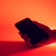 A hand holding a phone in a red background with shadows