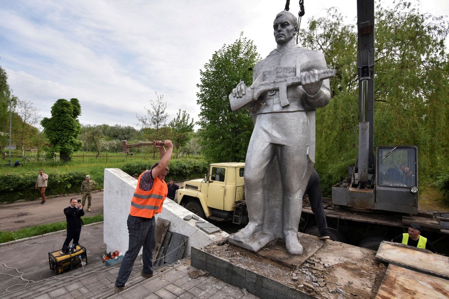 A person swings a hammer at the base of a statue of a soldier.