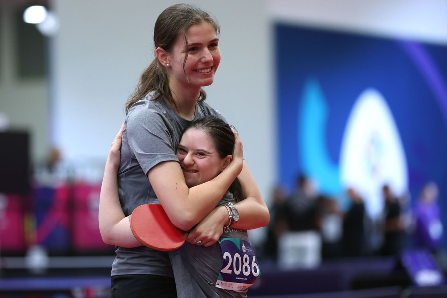 Two athletes embrace after winning a table tennis match.