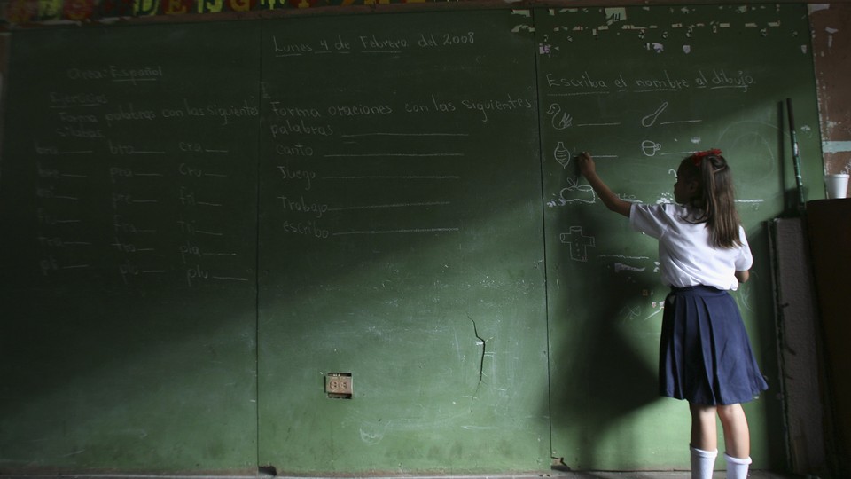 A child writes on a large chalkboard. Half the image is in shadows.