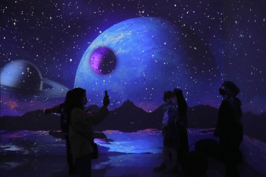 People take a photo in a dark room with walls illuminated by images of moons and planets.