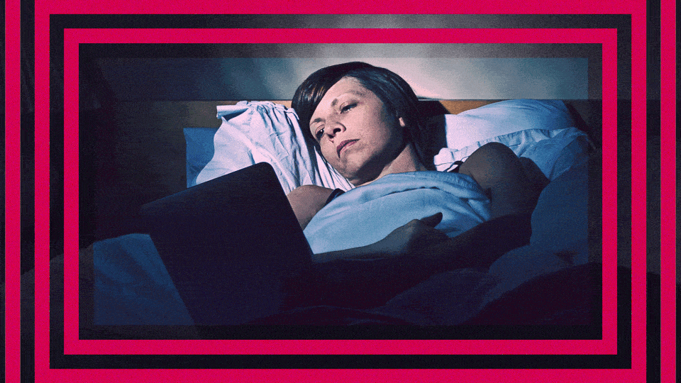 A woman lies in bed looking at a flickering screen