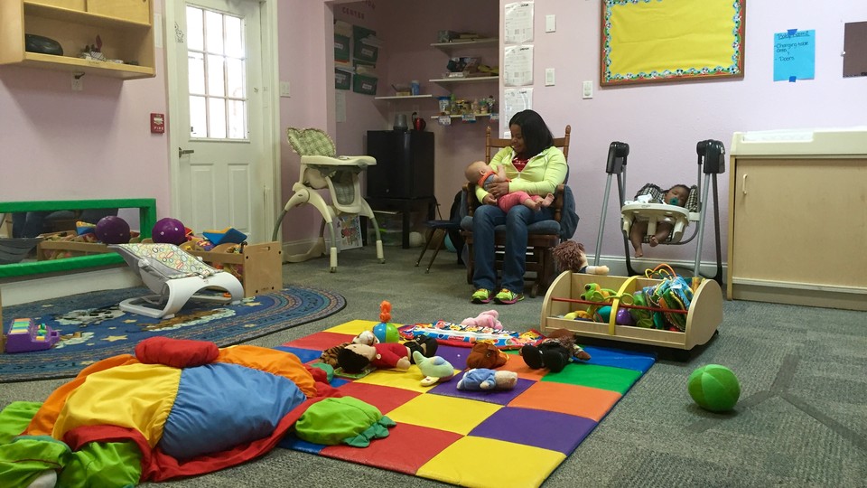 A woman holds a baby in a room filled with colorful toys and rugs.