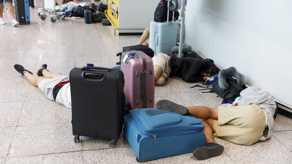 people sprawled out on an airport floor, along with carry-on suitcases