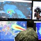A man in camouflage stands in front of computer screens showing images of Hurricane Irma. 