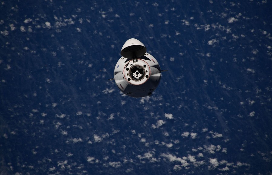 A view of a small spacecraft above distant clouds and Earth.
