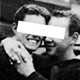 A grainy black-and-white image of two men embracing with a white rectangle covering their eyes