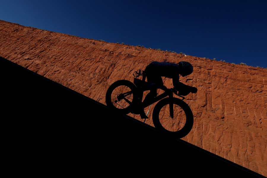 A racer rides a bike near a sheer rock wall.