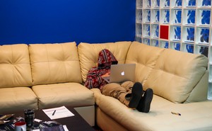 A person sits on a couch asleep with a laptop on his lap