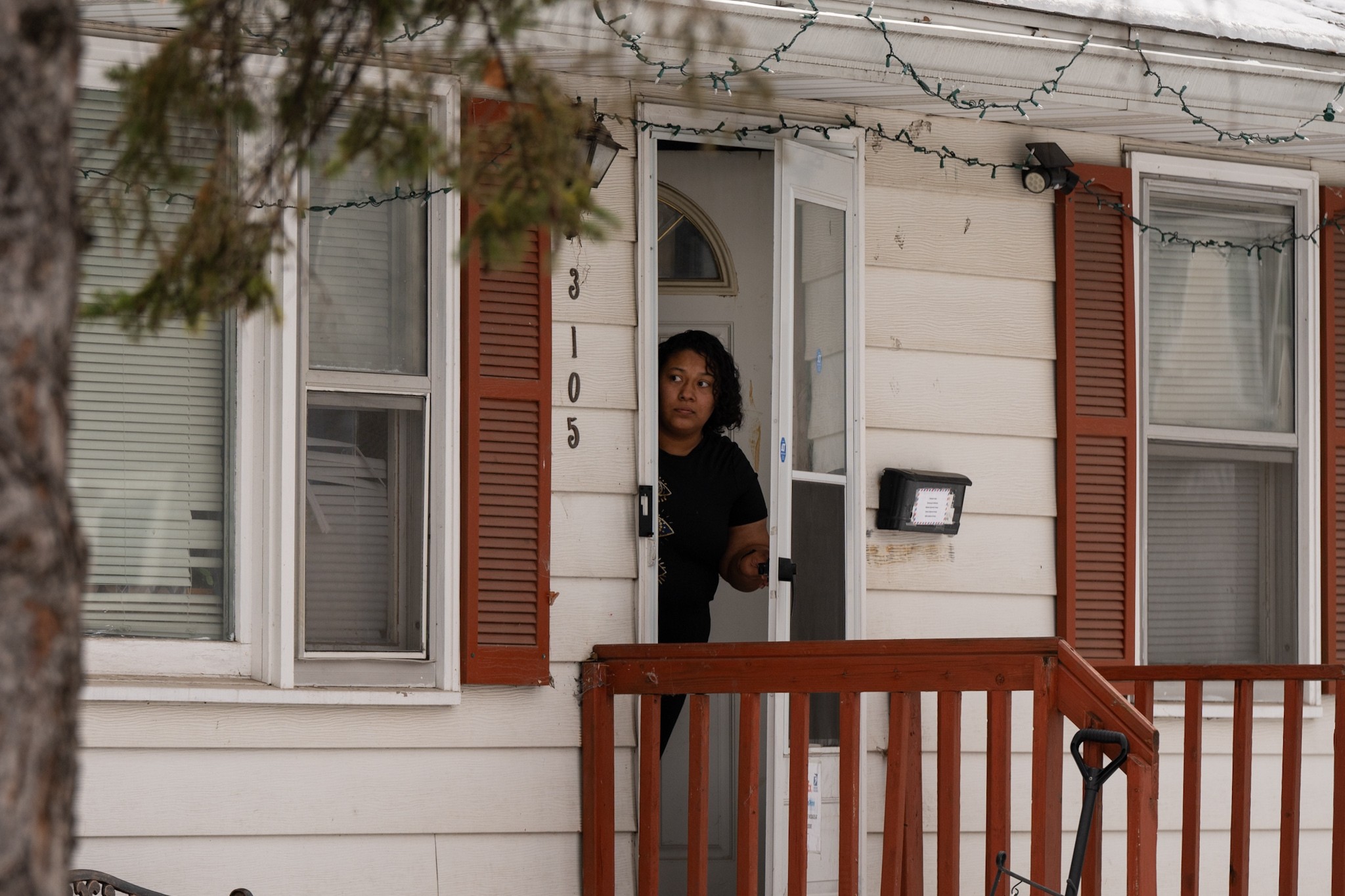 A person looks out of the front door of a house during an immigration raid