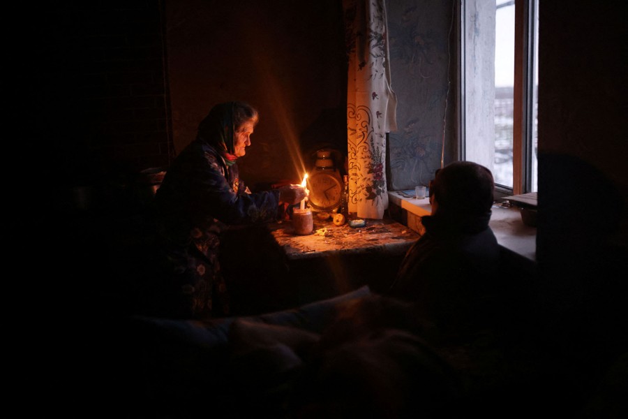 A woman lights a candle in a dark room, near a window.