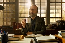Bob Odenkirk as Hank, a professor sitting at desk with a Railton College mug