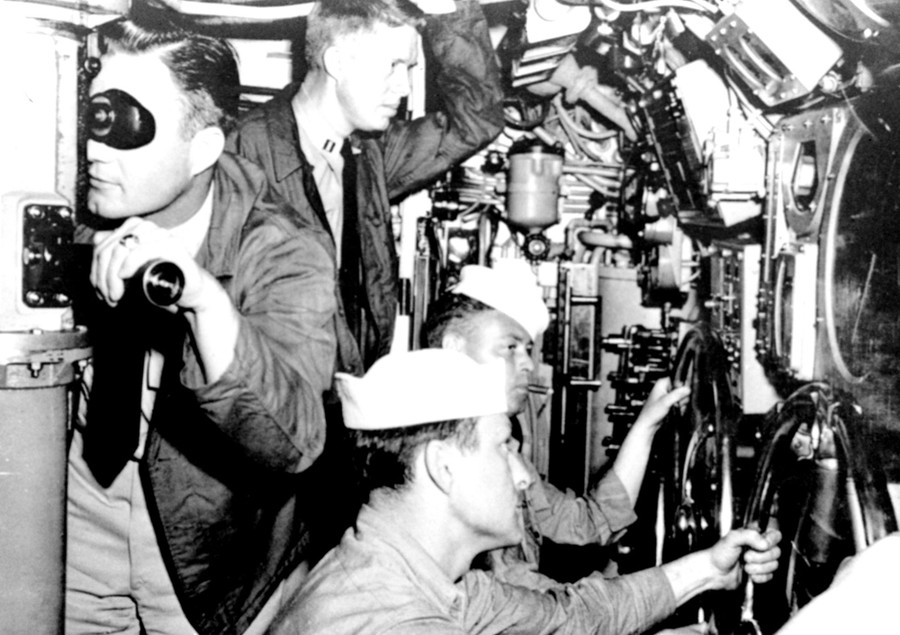 A black-and-white photograph of four men inside a submarine. The one standing and watching is Jimmy Carter.