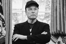 Elon Musk stands with his arms crossed.