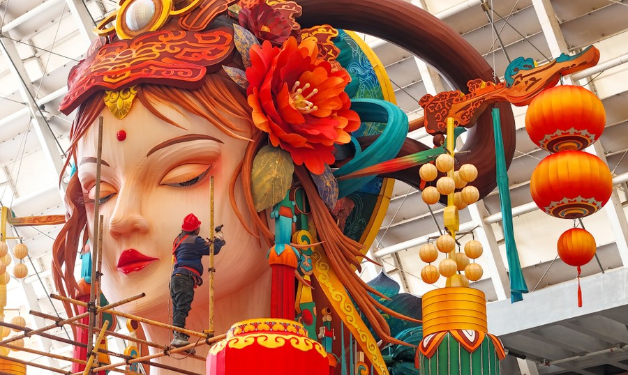 A worker sets up a giant lantern in the shape of a woman wearing an elaborate headdress.