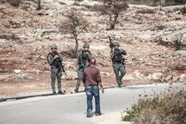 A man faces three armed Israeli soldiers on a road.