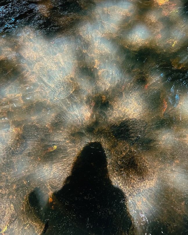 Shadow of woman above rippling, colored water
