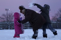 An adult comforts one child while another throws a snowball behind them. 