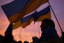 A crowd waving Ukrainian flags in front of sunset sky.