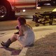A young woman sits on a curb in Las Vegas, with an EMS vehicle behind her