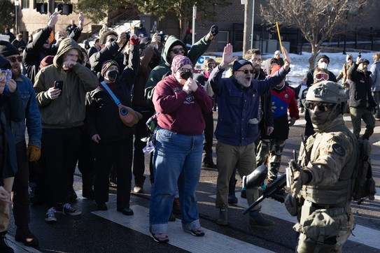 A group of people stand together in a street, confronting masked federal officers during an immigration raid.