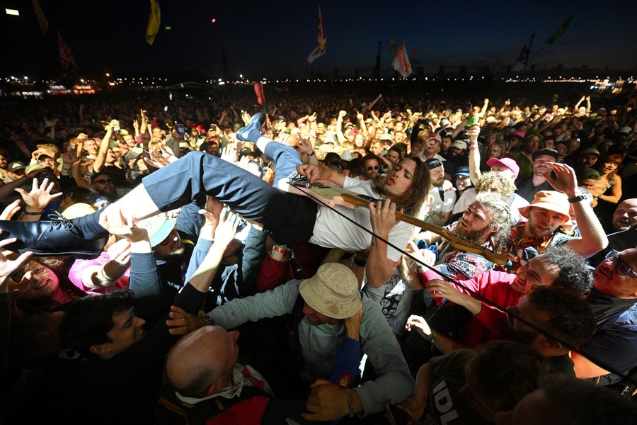 A musician plays guitar while lying on his back, being passed around over the heads of a large crowd.