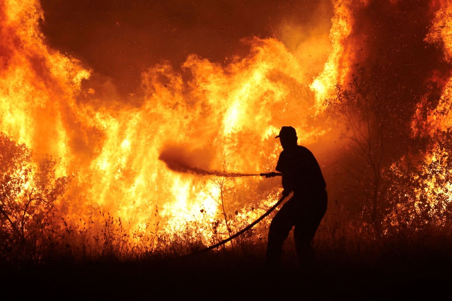 A person sprays water from a hose into a wall of flame during a wildfire.