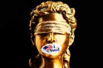 Lady Justice with an "I Voted" sticker covering her mouth