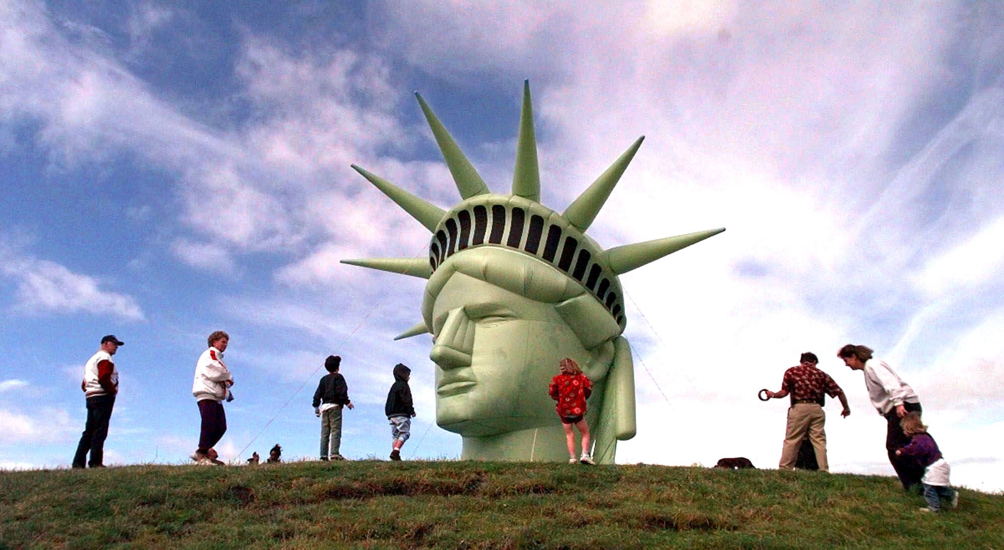 Visitors walk past a balloon replica of the head of the Statue of Liberty.