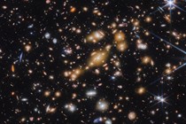 A field of galaxies on the black background of space. In the middle is a collection of dozens of yellowish galaxies that form a foreground galaxy cluster.