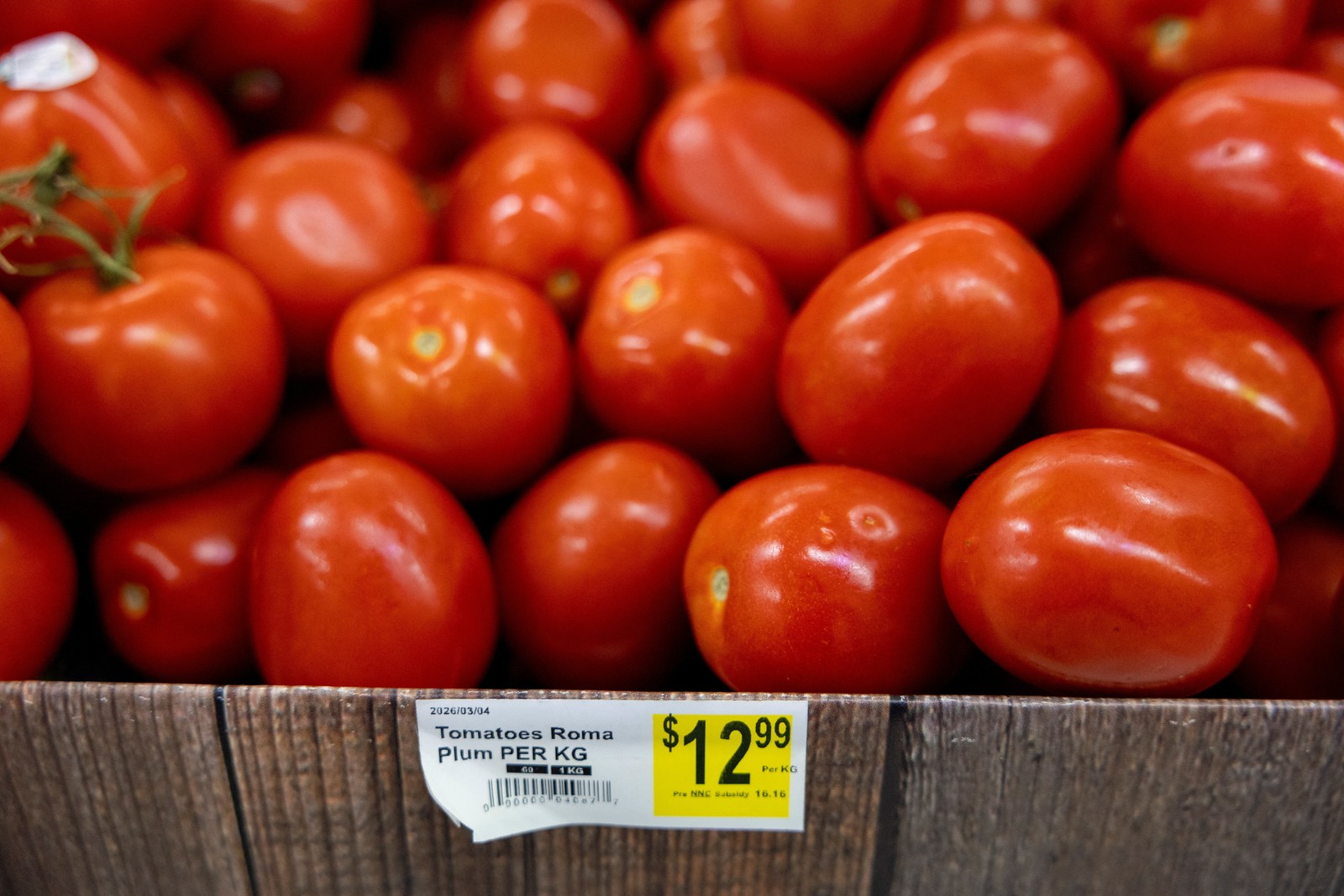 A pile of plum tomatoes, priced at $12.99 per kilogram in Canadian dollars.