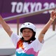 A young skateboarder raises her arms in celebration.