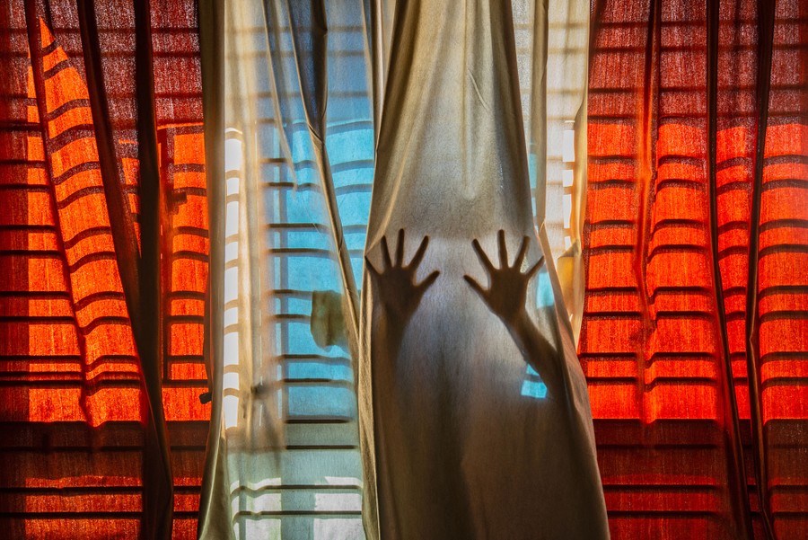 The silhouette of a person's hands is seen behind curtains.