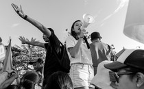 A black and white picture of a protest, focusing on a young woman with a megaphone.