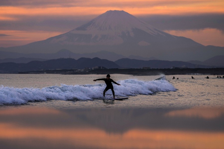 A surfer rides a small wave in front of Mount Fuji.