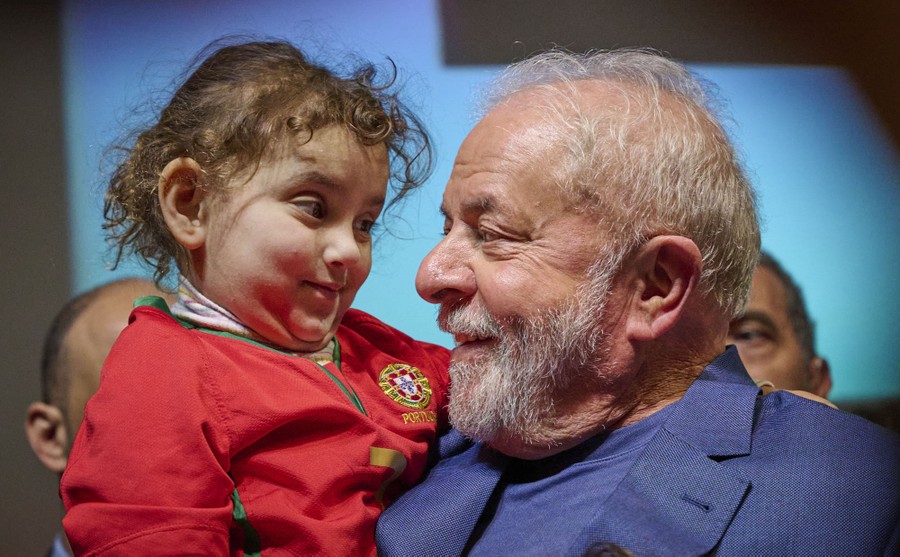 An older man smiles and holds a young child, as they look into each other's eyes.