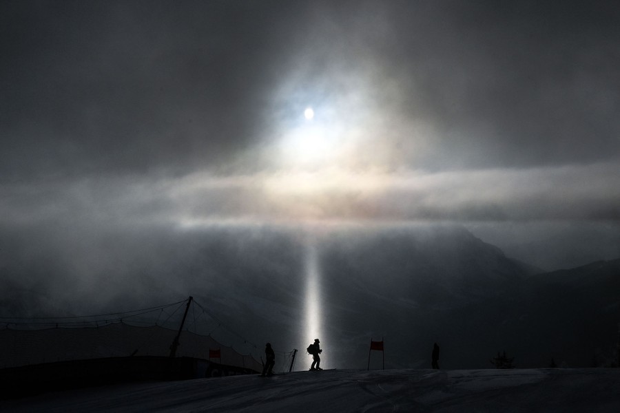 A person is visible on a ski slope, silhouetted by a ray of sunlight coming through clouds.