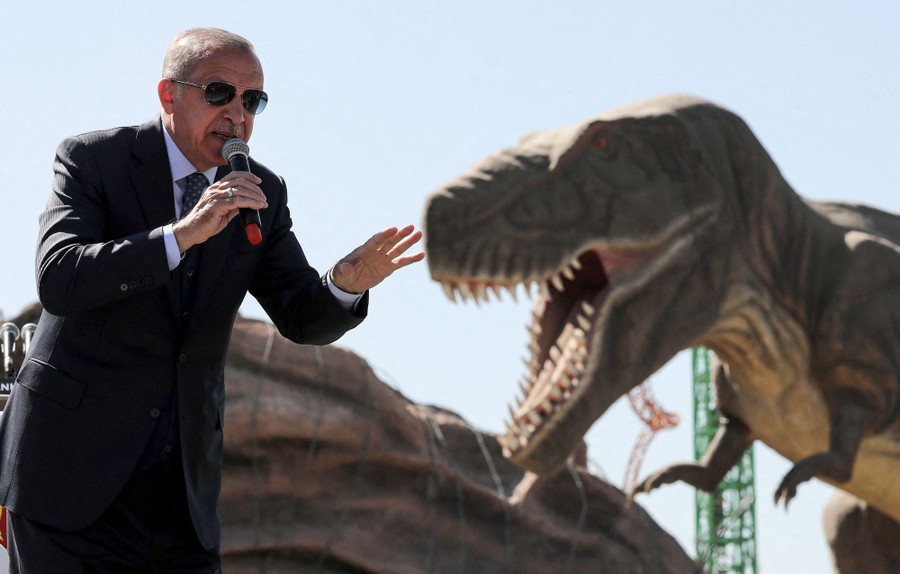 Turkish President Recep Tayyip Erdogan delivers a speech in front of a large dinosaur statue.