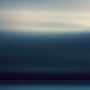 A long exposure of a passing storm over the horizon of the Pacific Ocean off the Oregon coast.  The long exposure renders the clouds as an abstract blur of motion and color and the setting sun highlights the higher clouds with a warm glow while the lower clouds are dark and brooding.