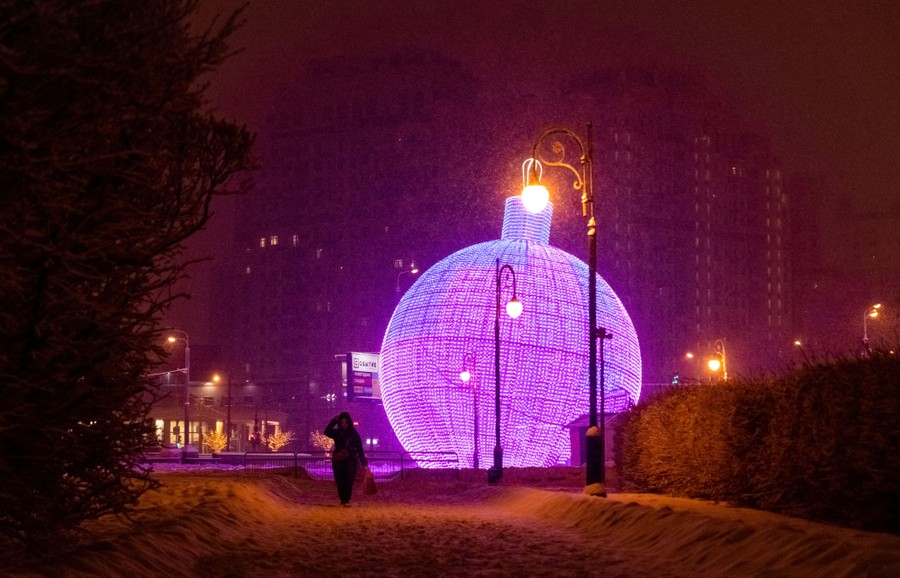 A person walks in a park at night, past a large illuminated Christmas ornament.
