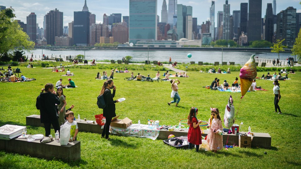 A birthday party in a park on a sunny day, with people relaxing in the background an urban skyline in the distance