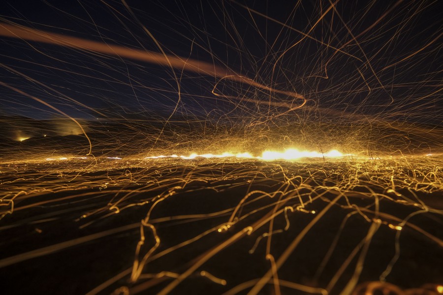A long-exposure image of wind-whipped embers at night, which appear as wiggling and bouncing streaks of light