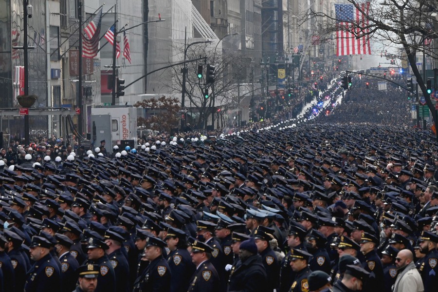Thousands of uniformed officers stand at attention lining a city street.