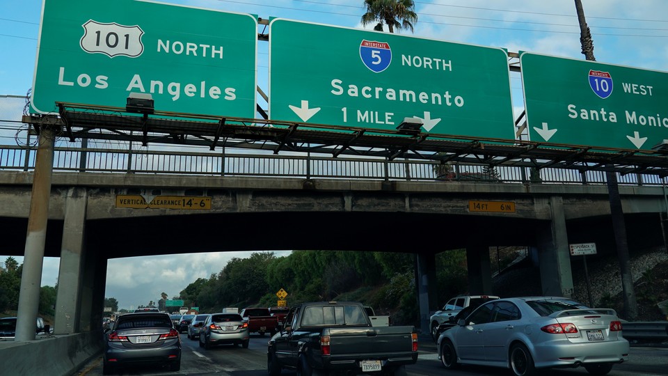 Morning traffic makes its way along a freeway interchange in Los Angeles. The traffic signs read Los Angeles, Sacramento, and Santa Monica.
