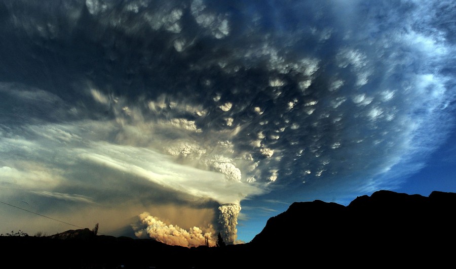 A cloud of ash billows from a volcano, spreading out into a huge cloud across much of the sky.