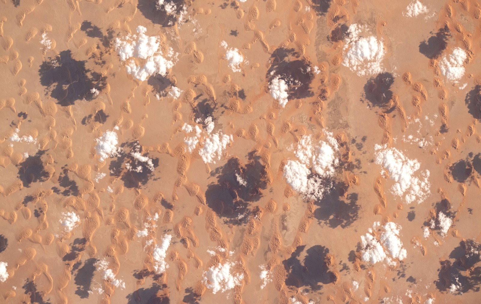 Sparse clouds pass above sand dunes, seen from far above.