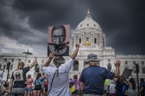 A group of protesters seen from behind raising signs and their fists, in front of the state capitol in St. Paul, Minnesota, in 2022