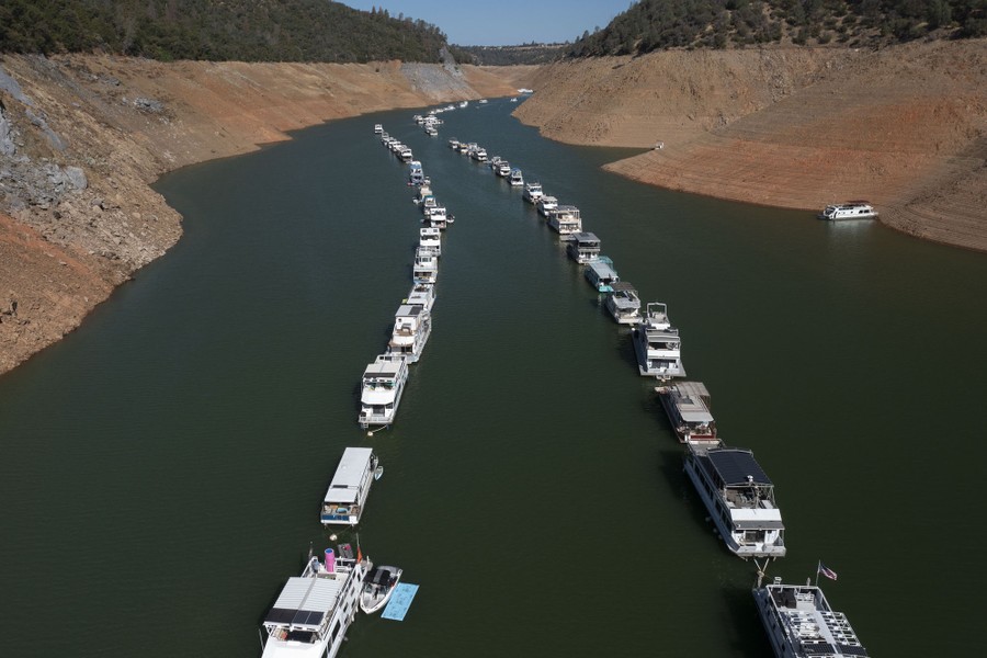 Dozens of boats sit in two lines, floating in a reservoir that is shrinking, exposing steep banks.