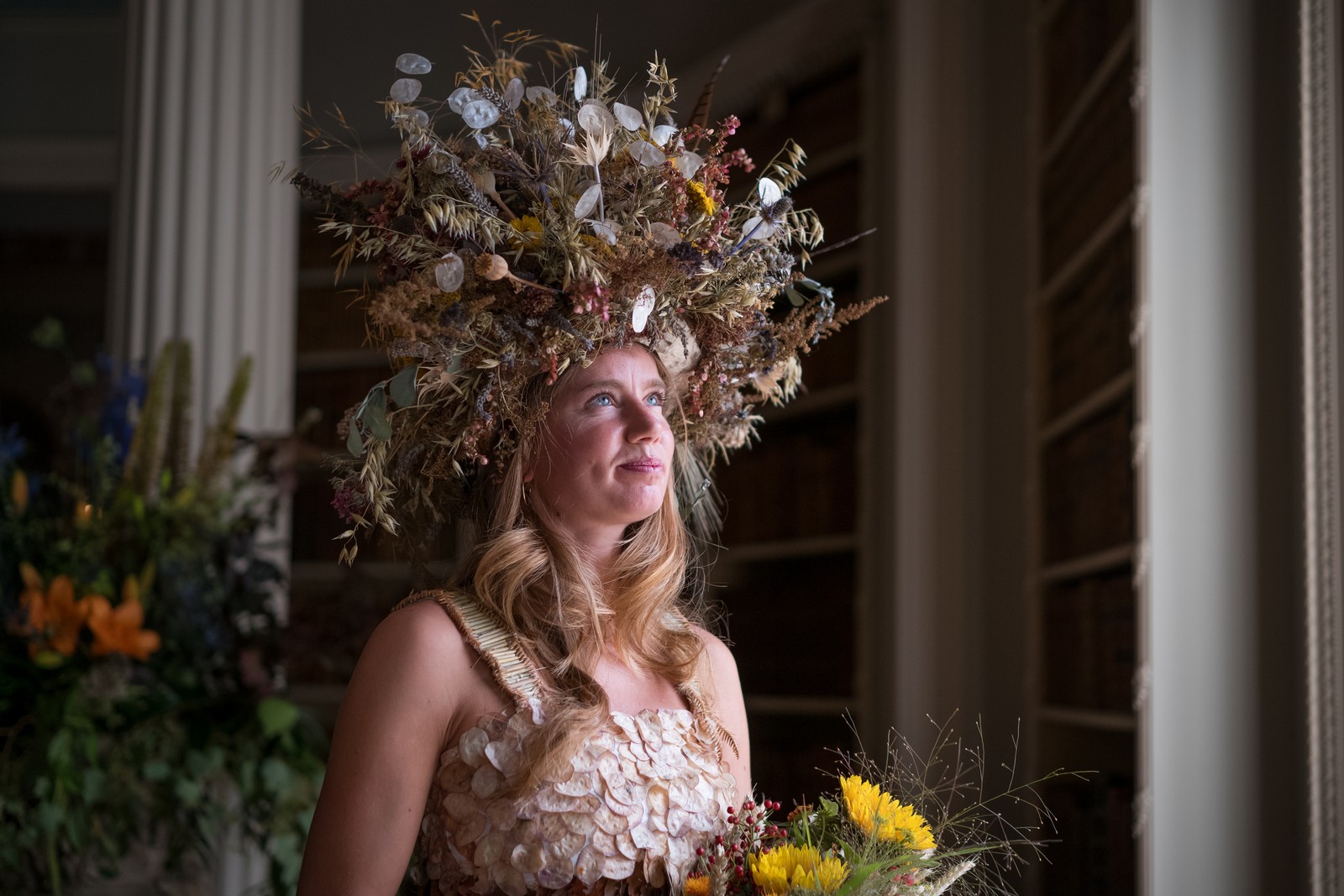 A model poses, wearing a dress and headgear adorned with autumnal foliage.