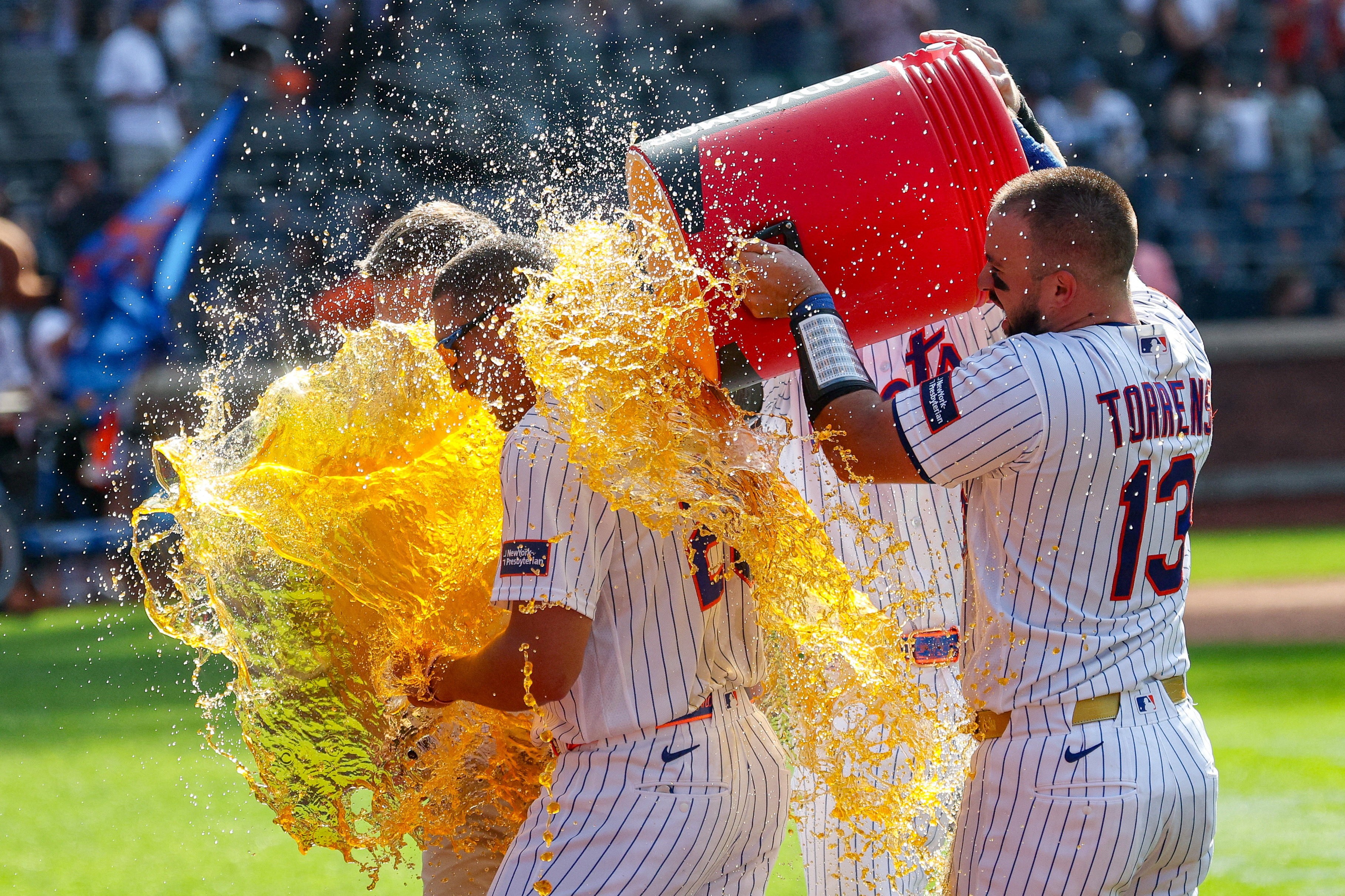 Baseball players dump a cooler full of orange sports drink on a teammate in celebration.
